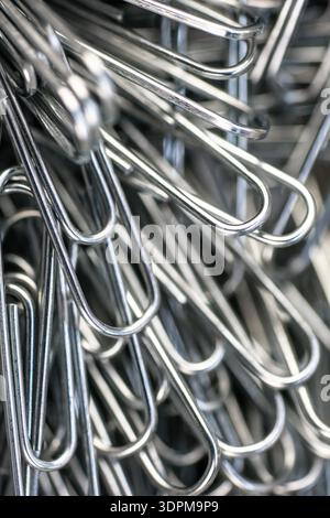 The scene shows many metal paper clips lying close together. The shiny surface reflects light. The paper clips are in different positions and angles. Stock Photo
