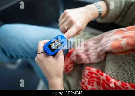 Woman resting at home using pulse oximeter to monitor blood oxygen levels and pulse rate. Stock Photo