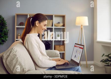 Smiling woman freelancer working on laptop at home, managing budgeting and savings Stock Photo