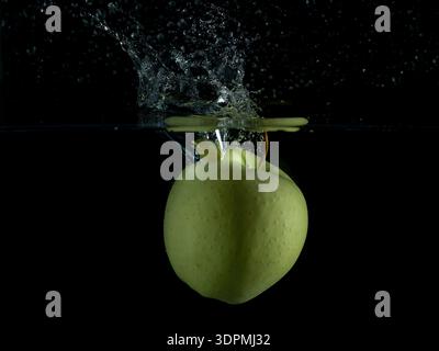 A green apple falls into the water, making a big splash Stock Photo