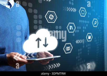 Hands holding tablet with cloud icons showing data transfer in a tech workspace during day Stock Photo
