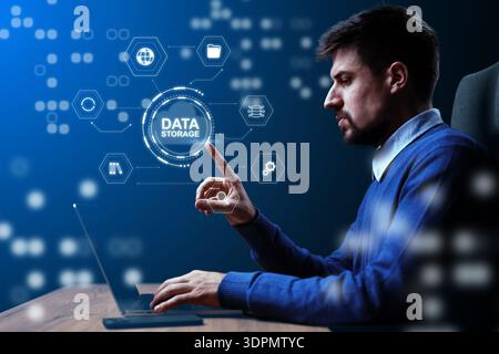 Man works at a laptop while interacting with data storage icons in a dark room Stock Photo