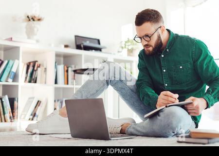 Millennial Guy Writing Taking Notes Looking At Laptop At Home Stock Photo