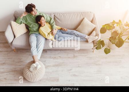 Happy relaxed millennial Asian man and woman cuddling on couch in living room, top view Stock Photo