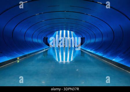 Futuristic blue illuminated interior space with blue illuminated escalators, curved tunnel and reflective floor in Chengdu city, China. Symmetry Stock Photo
