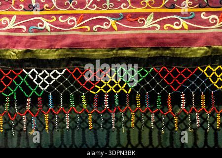 Colorful embroidered textile border with ornate floral trim and beaded fringe on dark fabric, traditional decorative pattern, close-up background. Stock Photo