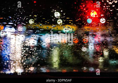 Rain drops on glass with colorful city lights bokeh at night Stock Photo