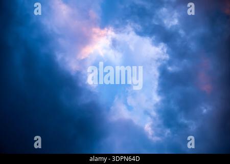 Dramatic sky full of dark clouds in bad weather before a big storm rain with a patch of light blue sky in center. Light emission from the Edge of Stock Photo
