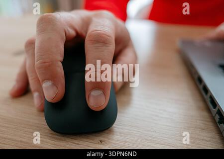Male hand resting on a wireless mouse and clicking, second hand typing on laptop. Modern workplace environment. Suitable for business, freelance Stock Photo