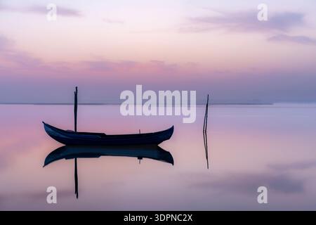 Minimalist landscape of a solitary boat floating on a calm lake at sunset, with soft pastel tones and perfect reflections creating a peaceful and medi Stock Photo