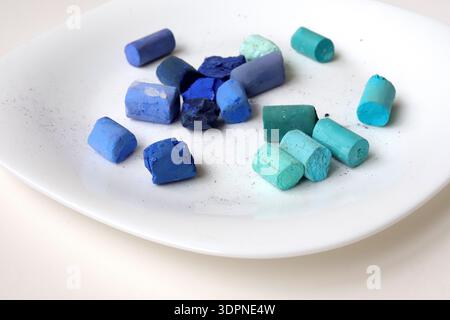 Blue and turquoise soft pastel crayons on a white plate. Art supplies for painting and drawing. Stock Photo