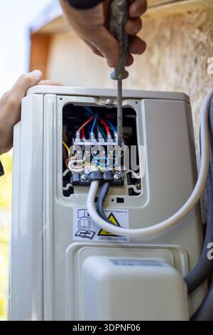 Installing the air conditioner external unit. A worker uses a screwdriver to connect the air conditioning system electrical control cable. Stock Photo