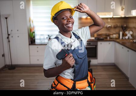 Smiling african american craftswoman holding cordless drill in kitchen Stock Photo