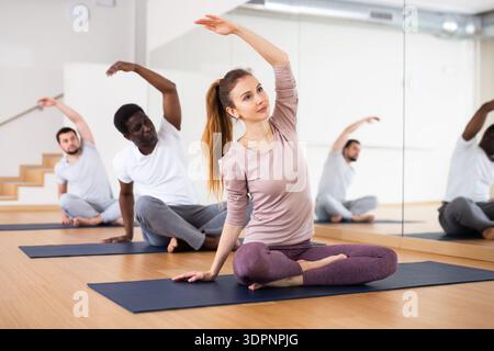 Woman doing Padmasana with side stretch during group yoga workout Stock Photo