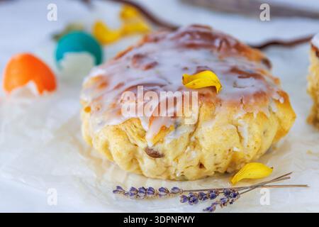 Close up of glazed easter bread on crinkled parchment with colorful cracked egg shells and a lavender sprig. Soft focus Stock Photo