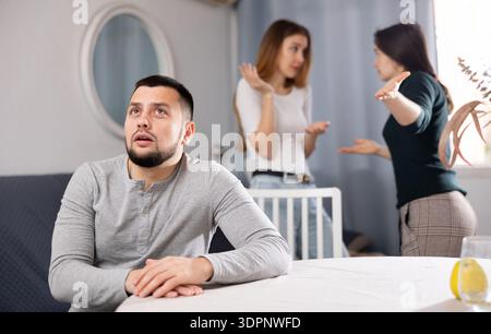 Offended man ignoring two women swearing at each other Stock Photo