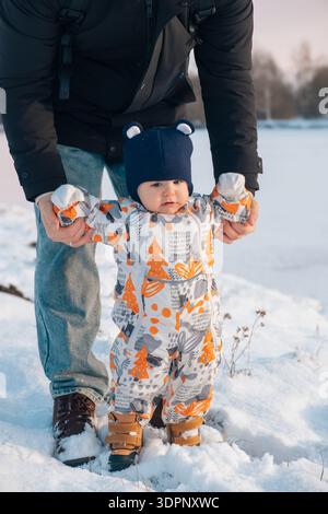 Baby in Snowsuit Held by Adult in Snowy Landscape Stock Photo
