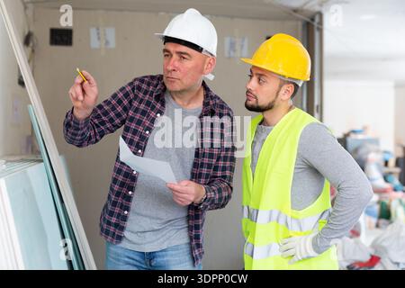 Adult designer with papers talking to contractor in building during renovation Stock Photo