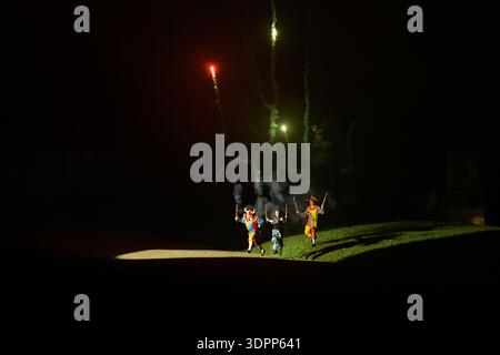 Unknown location - July 17, 2021: Three people dressed in colorful costumes are holding fireworks that shoot sparks and smoke into the night sky during an outdoor performance on a grassy field. Stock Photo