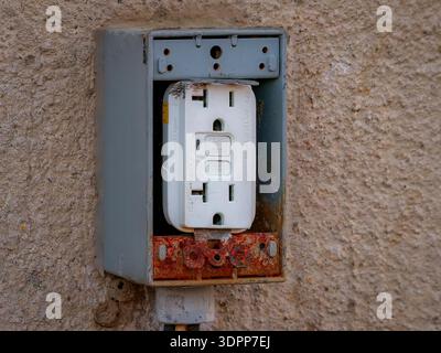 Weathered outdoor GFCI electrical outlet with rusted metal box mounted on stucco wall Stock Photo
