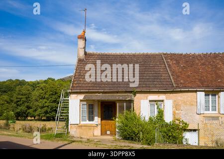 Beuvron, France - July 26, 2020: A traditional rural house with a tiled roof, chimney, white shutters, and a metal exterior staircase is seen under a blue sky, with trees and a field in the background. Stock Photo