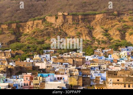 Bundi, India - March 20, 2022: The image shows densely packed historic buildings of the old town at the base of a hillside, with extensive stone fort walls running along the ridge above under daylight. Stock Photo