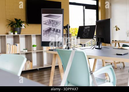 Workstation featuring dual monitors and laptop displaying plans on desk with mint-green chairs Stock Photo