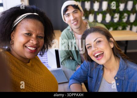 Diverse coworkers smiling for group selfie around wooden table with laptop chart in modern office Stock Photo