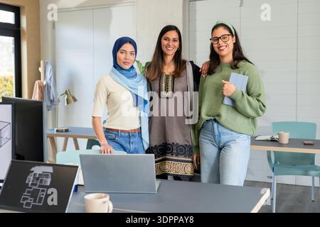 Diverse coworkers standing together in office meeting area holding tablet beside laptops on table Stock Photo