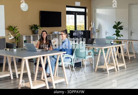 Diverse female colleagues reviewing floorplan designs on laptops and monitor in open office Stock Photo