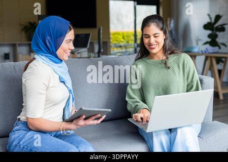 Diverse female coworkers collaborating on sofa in office using tablet and laptop Stock Photo