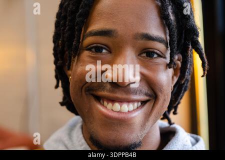 African American man with dreadlocks smiling and showing teeth in living room with warm light Stock Photo