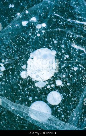 Macro view of trapped white methane gas bubbles suspended in deep blue, crystal-clear frozen lake ice. Stock Photo