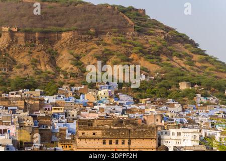 Bundi, India - March 20, 2022: The image shows densely packed historic buildings of the old town at the base of a hillside, with extensive stone fort walls running along the ridge above under daylight. Stock Photo