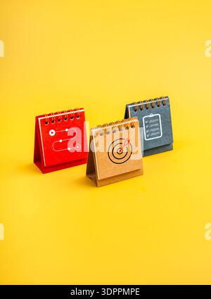 Three desk calendar with icons of checklist, target, and roadmap on vibrant yellow background. Work planning, productivity strategy, goal setting, wor Stock Photo