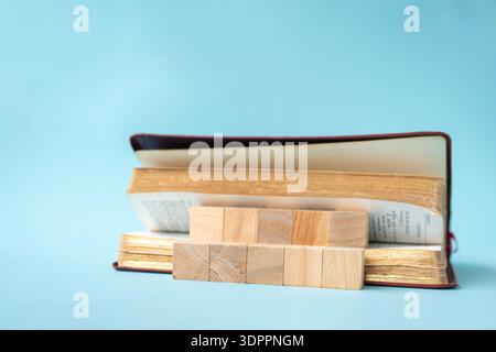 Square wooden blocks in between pages of a book. On light blue background. Stock Photo