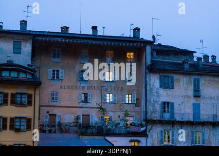 Ville de Verallo, Italy - September 27, 2020: Several multi-story residential buildings with weathered facades, balconies, and shuttered windows are visible at dusk, with interior lights illuminating some windows and rooftop antennas above. Stock Photo