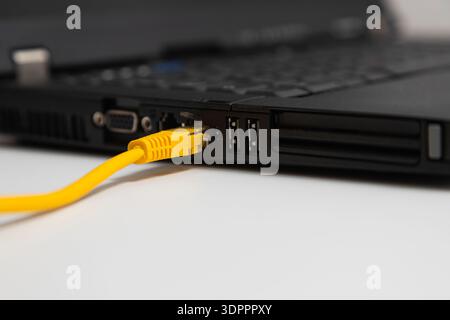 Yellow cable is connected to a laptop. The cable is plugged into the laptop's port, which is located on the side of the device. The cable is likely an Stock Photo