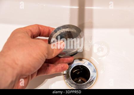 Hand removing a dirty sink drain stopper, revealing visible limescale buildup. Highlights household plumbing issues, maintenance, and cleaning needs Stock Photo