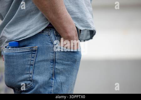 Man standing with hand in jeans pocket and plastic water bottle in back pocket, hand skin, close up Stock Photo