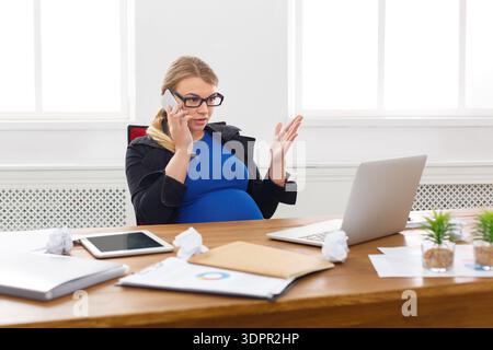 Pregnant Woman Talking on Phone in Office While Working on Laptop at Daytime Stock Photo