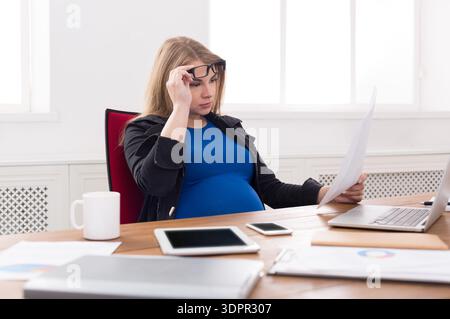 Pregnant Woman Working at Desk While Reviewing Documents in a Bright Office Environment Stock Photo