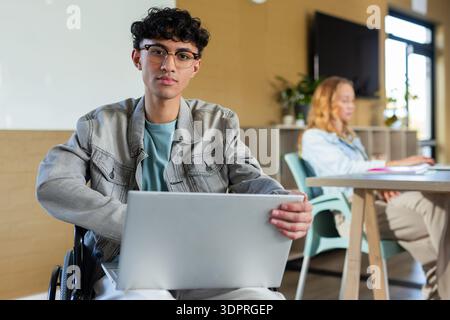 Diverse coworkers working independently at workspace using silver laptops, whiteboard, wheelchair Stock Photo
