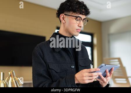 Man holding gray tablet in wood-paneled office featuring flat-screen monitor and brass desk lamps Stock Photo