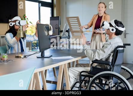 Diverse coworkers demonstrating VR simulation at open plan office with headsets wheelchair monitors Stock Photo