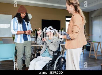 Diverse coworkers demonstrating virtual reality setup in lab with wheelchair, VR headset, tablet Stock Photo