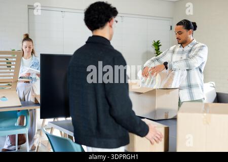 Diverse coworkers unpacking boxes and papers at meeting table with screen monitor, copy space Stock Photo