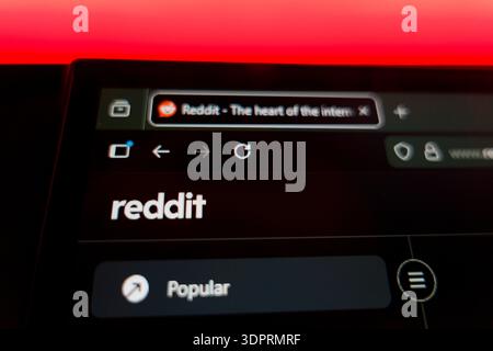 Close up of a computer screen showing the Reddit homepage with the official logo, browser tab, and navigation menu under a vibrant red light, represen Stock Photo