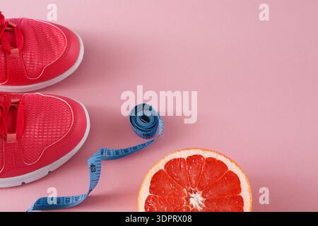 Bright Red Shoes Sit Next to a Measuring Tape and a Sliced Grapefruit on a Pink Background Stock Photo