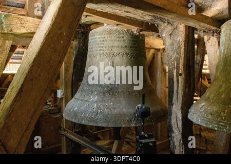 Eglise Saint Martin, France - July 23, 2020: A large metal church bell with an inscription is visible among wooden beams and support structures inside the bell tower of Eglise Saint Martin. Stock Photo